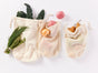 Three Conserve Organic Produce Bags by Coyuchi, filled with leafy greens, herbs, potatoes, onion, and pears, are displayed on a white background—ideal for a zero-waste lifestyle.