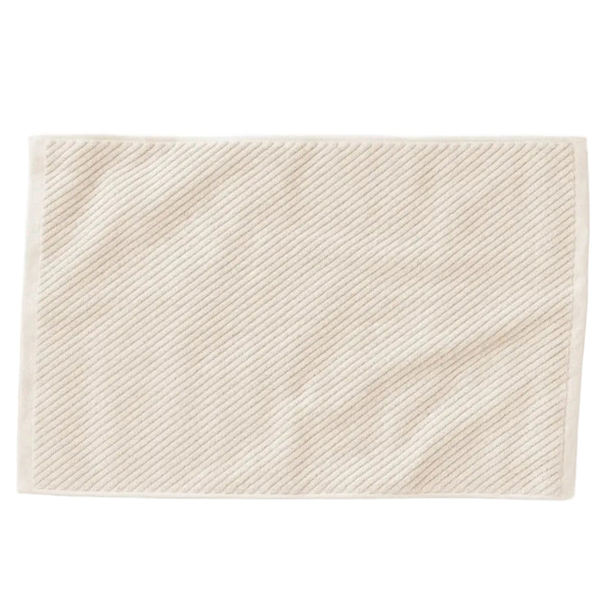 The Coyuchi Organic Twill Bath Mat from the Air Weight Collection is a cream-colored, rectangular mat with a subtle diagonal ribbed texture and plain border, crafted from organic cotton and shown on a white background.