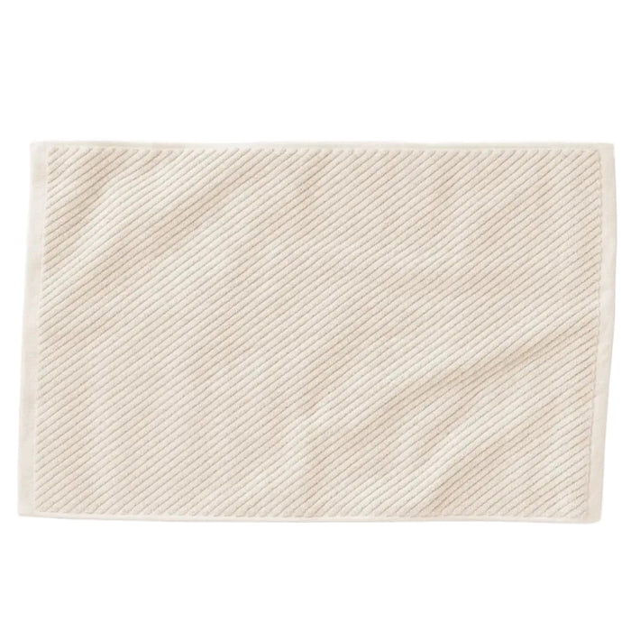 The Coyuchi Organic Twill Bath Mat from the Air Weight Collection is a cream-colored, rectangular mat with a subtle diagonal ribbed texture and plain border, crafted from organic cotton and shown on a white background.