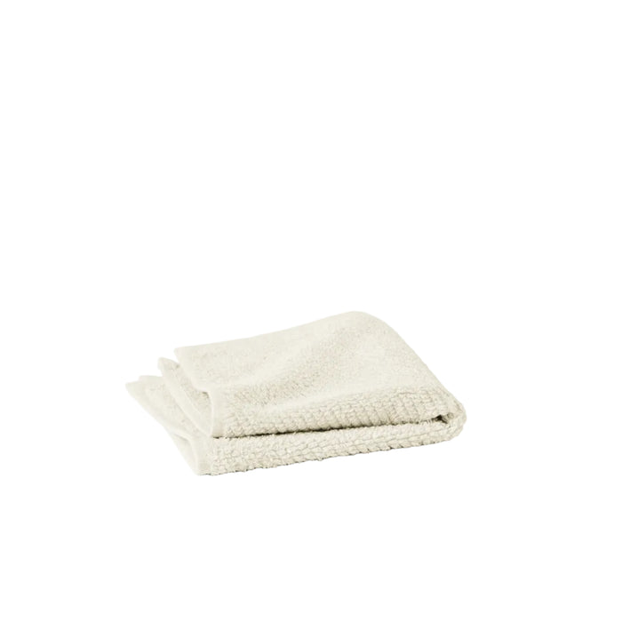 A neatly folded, light beige Organic Wash Cloth from Coyuchi's Air Weight Collection is placed on a white background.