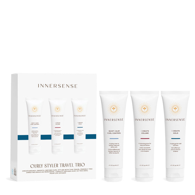 A box labeled Innersense Organic Beauty Curly Stylers Travel Trio stands next to three white tubes with the Innersense logo and orange accents: a nourishing styling cream, I Create Volume, and a medium-hold lotion or gel.