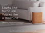 A modern living room featuring a white sofa and the Windmill Air Purifier Max by Windmill Air wrapped in bamboo beside it. Text reads: Designed to impress. Engineered to perform. Improve your indoor air quality with a purifier made to be seen.