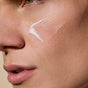 A close-up of a person's smooth skin with a small amount of Phil’s Daily Facial Moisturizer applied to the cheekbone, lips slightly parted.