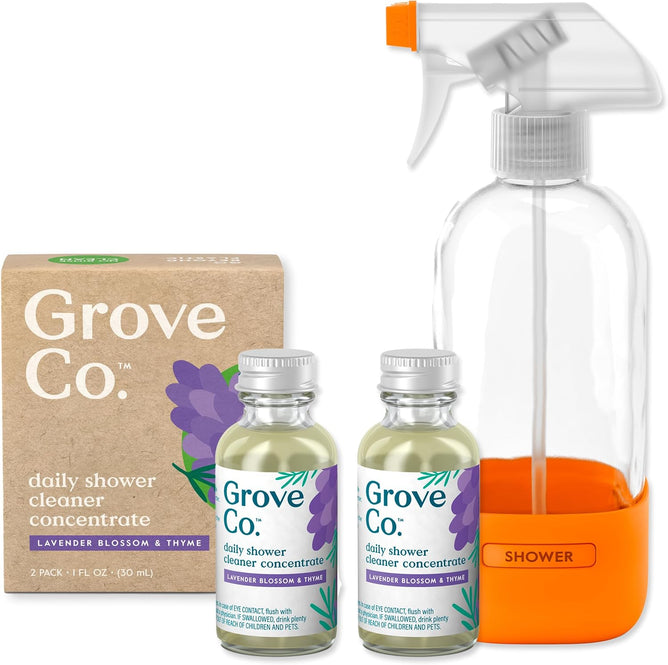 The Grove Co. Daily Shower Starter Pack includes a cardboard box, two glass bottles of shower cleaning concentrate with lavender labels, and a reusable glass spray bottle with an orange base labeled SHOWER.