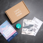 A flat lay of the Million Marker Exposure Test on a dark surface features a brown "Learn what's inside" box, teal-capped sample container, Exposure Test card for fertility-disrupting chemicals, clear plastic bag, and shipping label.