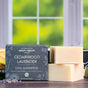 Two bars of Chagrin Valley Soap & Salve Dog Shampoo sit next to a dark green box labeled with Cedarwood Lavender and natural ingredients, set against a window showing lush green foliage outside.