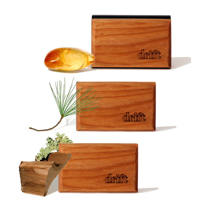 Drift’s 3-Pack Wood Car Air Freshener Starter Kit features three sustainably sourced wood blocks engraved with drift, plus a golden resin droplet, pine needle branch, and green lichen-covered wood, all displayed on a white background.