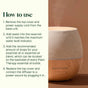 A Plant Therapy Drift Linen Diffuser, crafted from wood and cloth, rests on a brown background and emits a soft ambient glow. Step-by-step instructions for using the Drift Linen Diffuser are provided on the left, guiding users to add water, essential oil, and plug in the device.