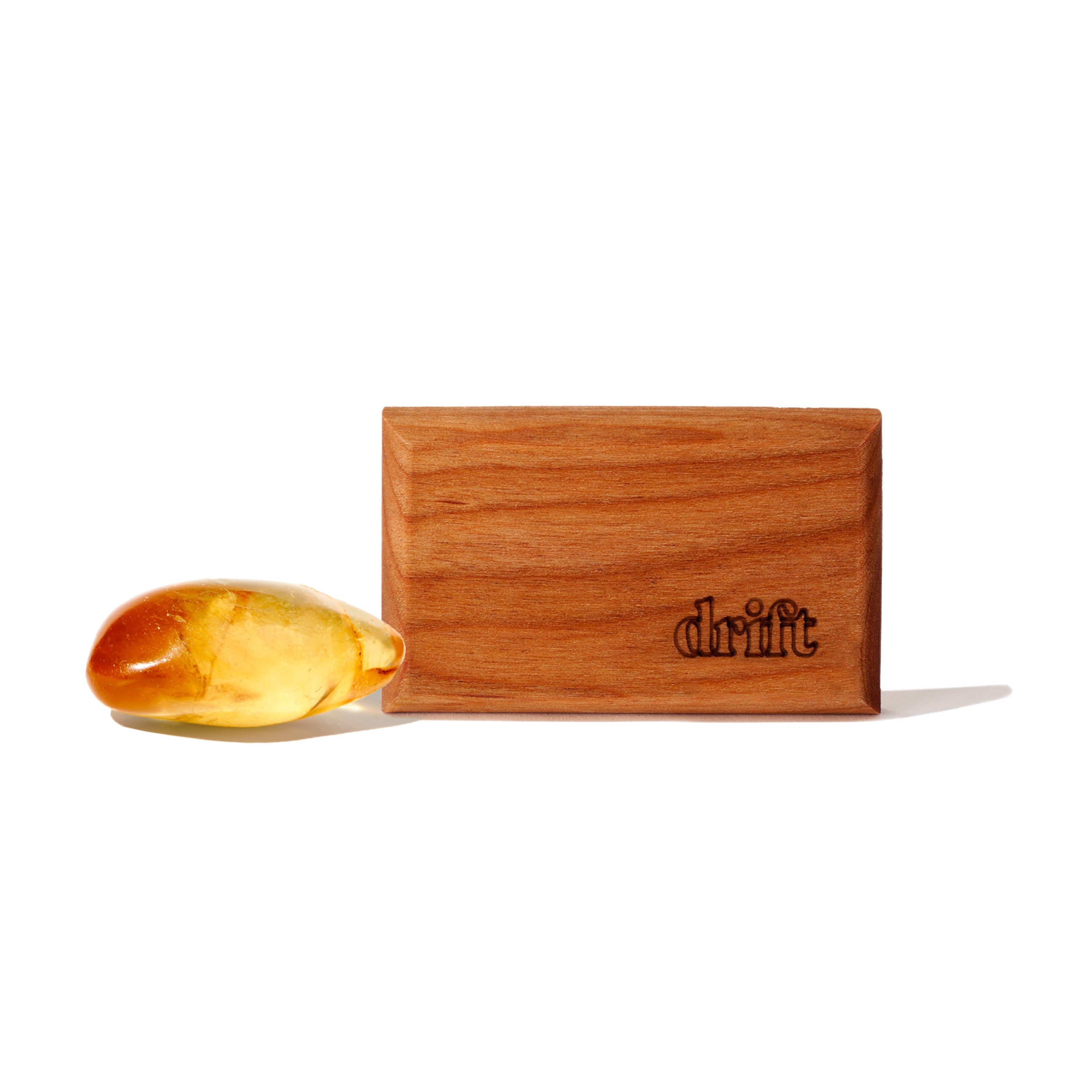 The Drift Wood Car Air Freshener Refill, a rectangular wooden piece engraved with drift, is shown beside an amber stone on a white background, suggesting premium scents and essential oil blends.