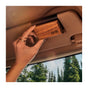 A hand attaches the Drift Single Wood Car Air Freshener Starter Kit to a cars sun visor. Made from sustainably sourced wood and essential oils, it delivers nature-inspired freshness as trees and sky are visible through the windshield.