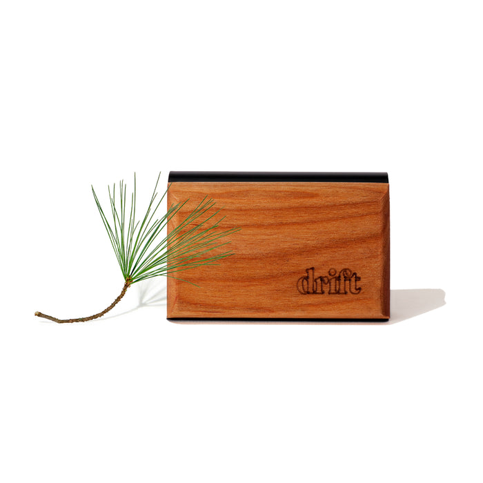 The Drift Single Wood Car Air Freshener Starter Kit, featuring a rectangular sustainably sourced wooden block engraved with drift, is displayed beside a pine twig on a white background.