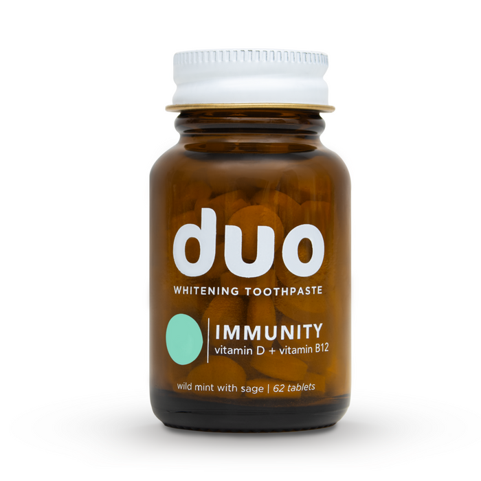 A brown glass bottle of duo Toothpastes Vitamin D Toothpaste Tablets holds 62 pieces, enhanced with vitamins D3 and B12 for better mucosal absorption. The label features wild mint and sage, with a green circle design and a white cap.