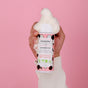 A hand in a white sweater holds a pink bottle of Everyday For Future Moisturizing Cleansing Foam, an organic face cleanser, against a pink background, with foamy cleanser overflowing from the top.