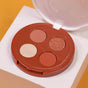 The Coffee Oil Infused Pigmented Eyeshadow Palette by Everyday For Future, a round quad with matte beige, matte brown, shimmery copper, and champagne shades in a red compact, sits on a white block against a yellow background.