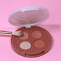 The Coffee Oil Infused Pigmented Eyeshadow Palette by Everyday For Future, featuring two matte and two shimmery shades, sits on a pink background as a makeup brush touches the matte mauve color.