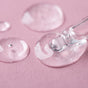 A close-up shows the Everyday For Future Moisturizing Face Serum with Hyaluronic Acid being dispensed from a glass dropper onto a pink surface, with drops scattered around, showcasing its visible hydration boost.