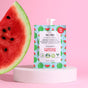 The Hydrating Watermelon Face Mask by Everyday For Future, with vibrant watermelon graphics, sits on a white pedestal against a pink background. This vegan skincare pouch offers 12 uses with natural ingredients and is paired with a large watermelon slice on the left.