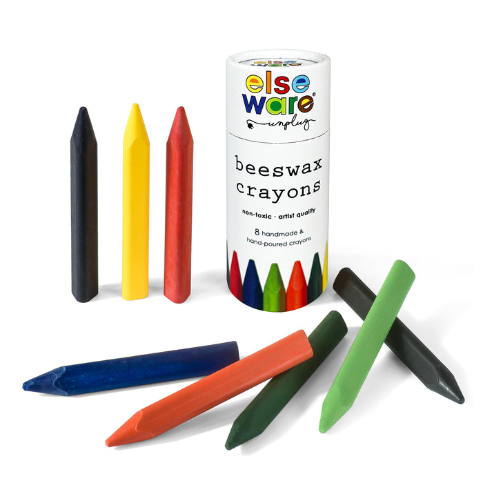 A set of colorful, non-toxic Beeswax Crayons by Elseware Unplug are shown upright and lying down beside a cylindrical container. The crayons come in red, yellow, blue, green, orange, and black.