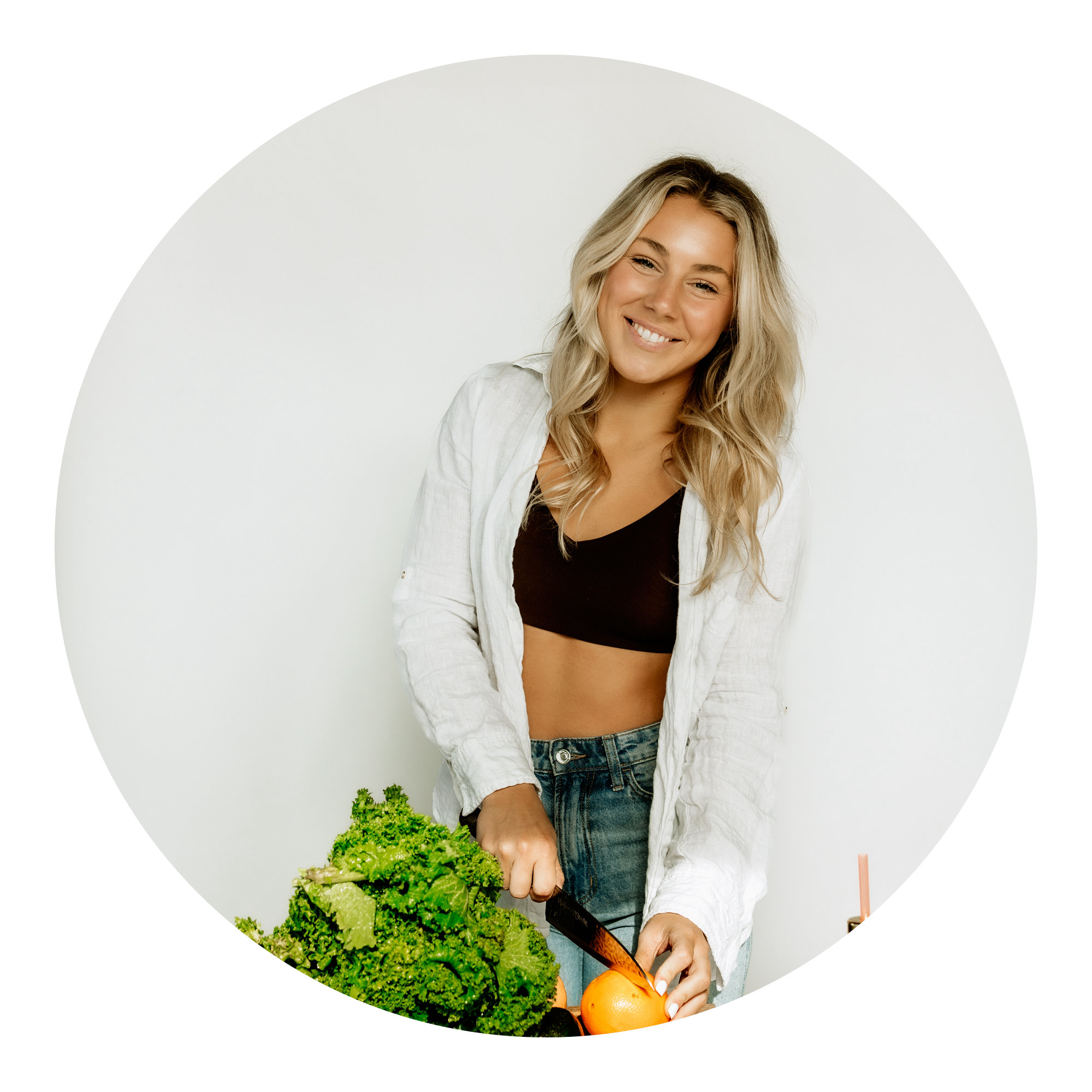 A smiling woman with long blonde hair wearing a white shirt and black top stands against a white background, slicing vegetables including leafy greens and an orange bell pepper.