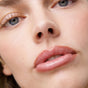 Close-up of a person's face highlighting their lips, nose, and blue eyes. Their glossy lips are defined with Ere Perez Acai Lip Pencil, while smooth skin and minimal makeup on lashes and brows complete the natural look.