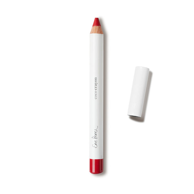 A red natural matte Coco Crayon Lipstick by Ere Perez, featuring a white body labeled “COCO CRAYON” and “Ere Perez,” is shown uncapped and lying to the right on a white background.