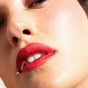 Close-up of a person's face with smooth, glowing skin and lips wearing Ere Perez Coco Crayon Lipstick in a hydrating red shade. The image highlights the detailed texture of both the skin and the lipstick on slightly parted lips.