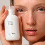 A person with dewy skin holds the Ere Perez Ginkgo Micellar Cleanser close to their face, highlighting clear, natural beauty—the ideal gentle cleanser for a refreshing sensitive skin routine.