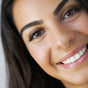 Close-up of a young woman with long dark hair and smooth skin, smiling brightly with well-groomed eyebrows enhanced by Ere Perez Jojoba Eye Pencil—perfect for sensitive eyes thanks to its soothing jojoba formula.
