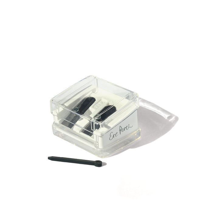 The Ere Perez Perfect Catch Duo Sharpener is a clear box with two black sharpeners for precise makeup pencil sharpening, plus a small black cleaning stick, all displayed on a white background.