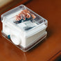 The Ere Perez Perfect Catch Duo Sharpener comes in a small, clear plastic box with a white base containing dried brown flowers and leaves—ideal for storing your sharpener or makeup pencils and maintaining precision.