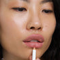 A person with smooth, glowing skin and a nose ring applies the Ere Perez Acai Lip Pencil to their lips, looking slightly downward.
