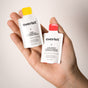 A hand holds two Everist hair care packets—The Shampoo Concentrate Sample with a yellow cap and a deep conditioning concentrate with a red cap—highlighting sustainable Everist products against a neutral background.