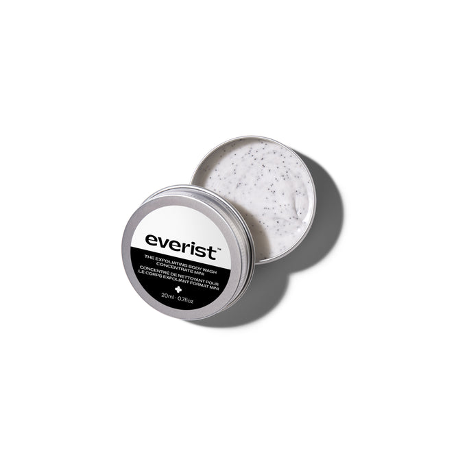 An open tin of Grove Collaborative’s The Exfoliating Body Wash Concentrate reveals its creamy white formula with dark exfoliating specks, showcasing skincare ingredients against a clean white background.