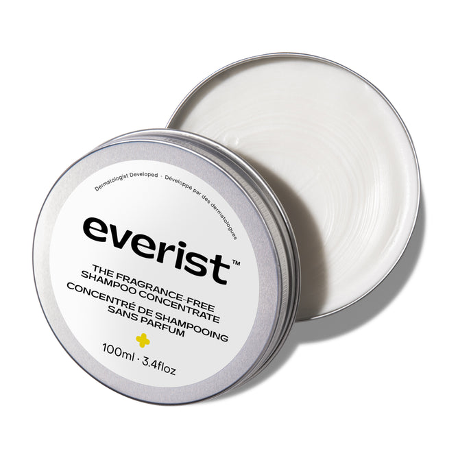 A round silver tin of Everist’s The Fragrance-Free Shampoo Concentrate sits with its lid partly open, showing creamy white formula inside. The 100ml label in English and French highlights its suitability for sensitive scalps.