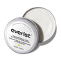 A round silver tin of Everist’s The Fragrance-Free Shampoo Concentrate sits with its lid partly open, showing creamy white formula inside. The 100ml label in English and French highlights its suitability for sensitive scalps.