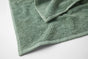 A close-up of a textured green Coyuchi Air Weight® Organic Towel highlights its soft, absorbent surface and neatly stitched edges as it rests on a white background—ideal for anyone who values the plush comfort and superior absorbency of premium organic bath towels.