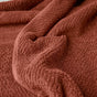 A close-up of a soft, textured Coyuchi Air Weight® Organic Towel in rust, showcasing its visible fibers and subtle fabric folds.