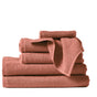 A neatly folded stack of four rust-colored Coyuchi Air Weight® Organic Towels, with a small towel draped over the top, set against a plain white background.