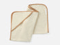 A soft, cream-colored bath mitt with tan trim and a small white COYUCHI tag is displayed on a plain white background—a perfect companion to the Cloud Loom™ Organic Baby Hooded Towel and Bath Mitt Set by Coyuchi for gentle, everyday baby care.