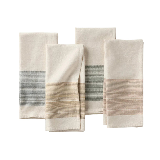 Four folded organic kitchen towels with woven stripe accents in blue, tan, green, and blush pink, arranged on a white background. These absorbent cotton towels are yarn dyed for rich, lasting color and effortless style in your kitchen.