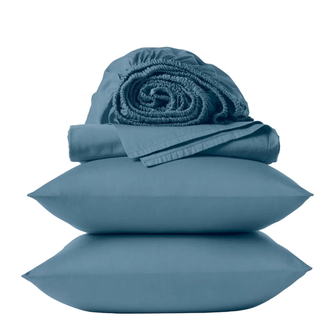 Two blue pillows are stacked with a folded blue sheet and a rolled fitted sheet on top, all from the Coyuchi Classic Organic Sateen Sheet Set, crafted from GOTS certified organic cotton, against a plain white background.