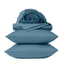 Two blue pillows are stacked with a folded blue sheet and a rolled fitted sheet on top, all from the Coyuchi Classic Organic Sateen Sheet Set, crafted from GOTS certified organic cotton, against a plain white background.