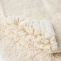 A close-up of Coyuchi’s Shag Organic Bath Rug in a soft, cream hue, with one corner folded to reveal both its plush shag surface and subtle ribbed underside—capturing the luxurious texture of this organically crafted bathroom essential.