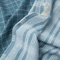 Two blue and white kitchen towels made from GOTS certified cotton: one with a checkered pattern and one with vertical stripes. Both sustainable kitchen towels are slightly wrinkled and overlapped, with a white hanging loop visible on the striped towel.