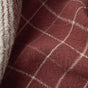 A close-up view of the Clarendon Organic Kitchen Towels by Coyuchi, featuring a maroon fabric with a white checkered pattern and a white-striped edge, highlighting the textured folds in GOTS certified cotton for sustainable kitchen linens.