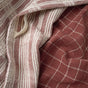 A close-up of two Clarendon Organic Kitchen Towels from Coyuchi—one featuring white and burgundy stripes, the other displaying a burgundy background with white grid lines—crafted from GOTS certified cotton. Designed for sustainable kitchen use, the overlapping towels highlight their eco-friendly materials and elegant patterns.