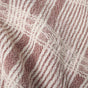 Close-up of a textured fabric with a woven pattern in cream and dusty rose, featuring intersecting vertical and horizontal lines that form a grid design. The material, from Coyuchi’s Clarendon Organic Kitchen Towels (Set of 4), is GOTS certified organic cotton and appears soft and slightly wrinkled.