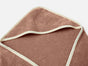 A soft, brown Cloud Loom™ Organic Baby Hooded Towel and Bath Mitt Set by Coyuchi, featuring a cream-colored trim, is folded at the corner to display its plush texture and detailed edging against a plain white background.
