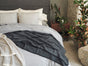 A neatly made bed with gray and cream bedding, featuring the Coyuchi Organic Crinkled Percale™ Sham, a black throw blanket, decorative pillows, and a bedside table holding potted plants in a cozy, modern bedroom. For added comfort and sustainability, the Organic Crinkled Percale™ Sham is crafted from GOTS Certified organic cotton.