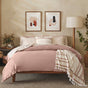 A neatly made bed is dressed in Coyuchi’s Organic Crinkled Percale™ Duvet Cover in blush pink, accompanied by patterned pillows and a striped throw. Two abstract art pieces hang above the bed, while plants, a floor lamp, and neutral-toned decor create a serene and inviting atmosphere.